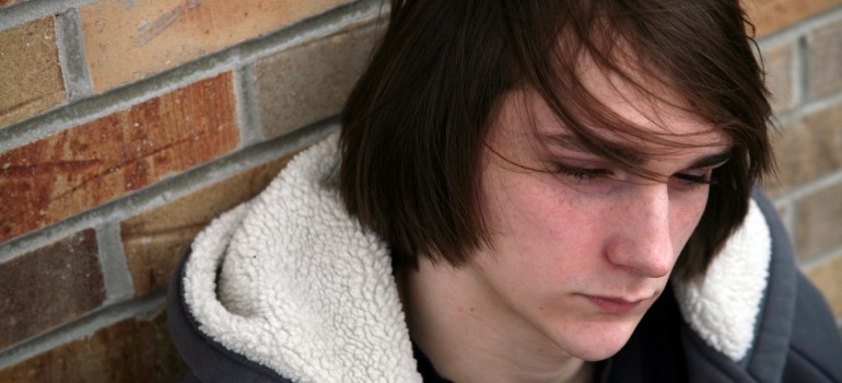 closeup of sad teen boy with great hair by brick wall