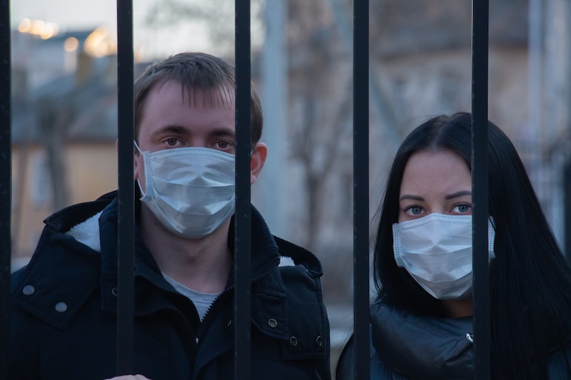 Two people wearing masks behind bars