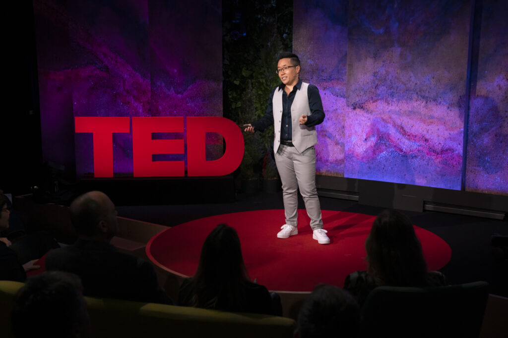 Dr. Jiaying Zhao wearing semiformal attired on stage at TED@DestinationCanada Institute. Behind her, the TED logo is in red as the backdrop.