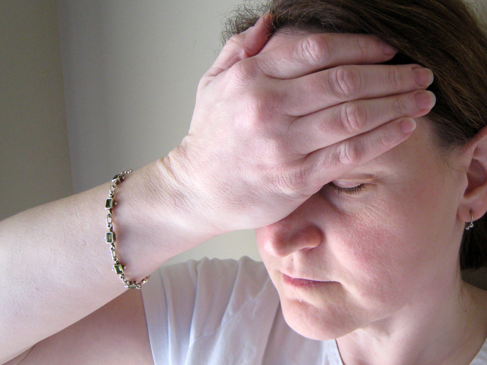 A white woman appears distressed and is feeling pain in her head. She places her right hand on her forehead, indicating her distress.
