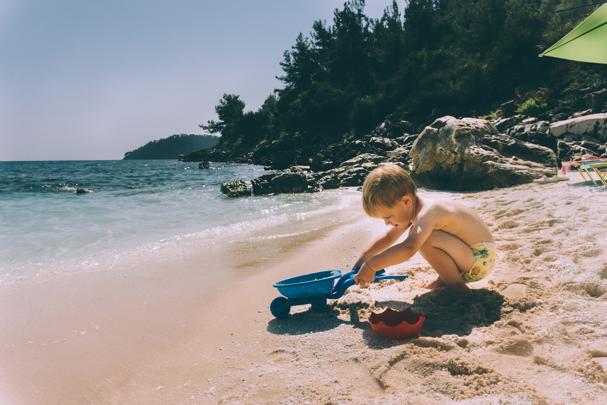 A caucasian young child on the beachside playing with sandcastle building tools.