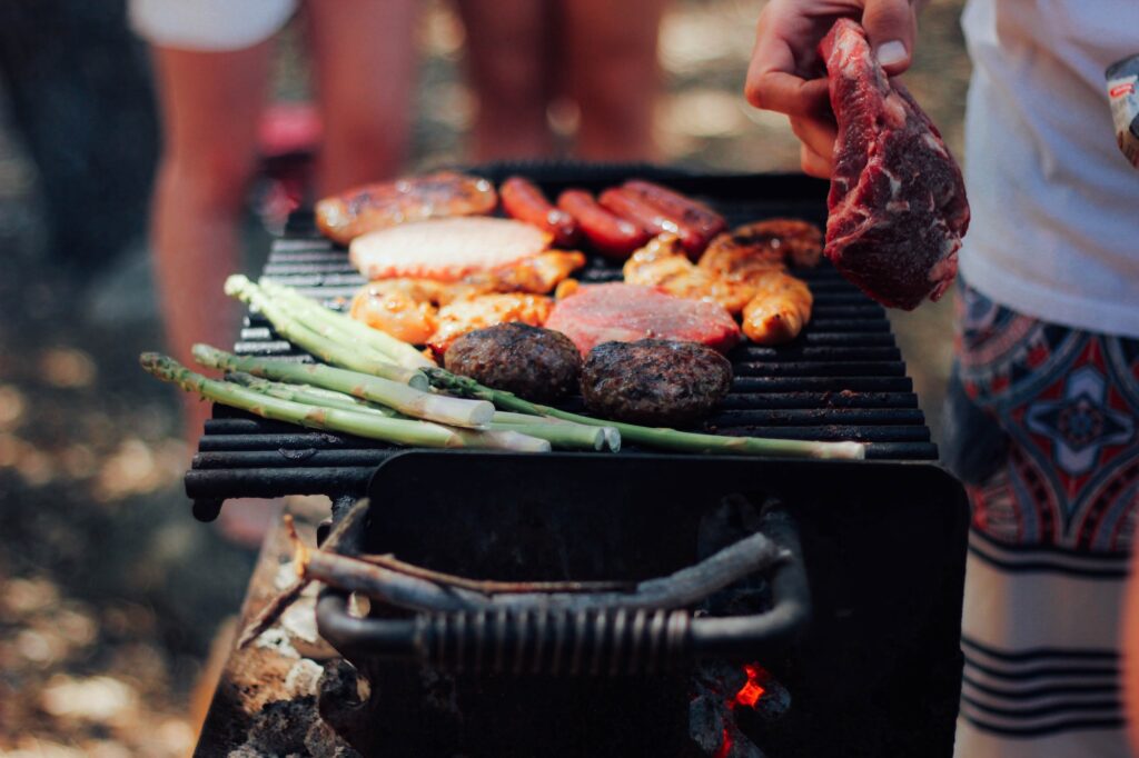 a grill with burger meat, asparagus, steak, sausages and marinated meats