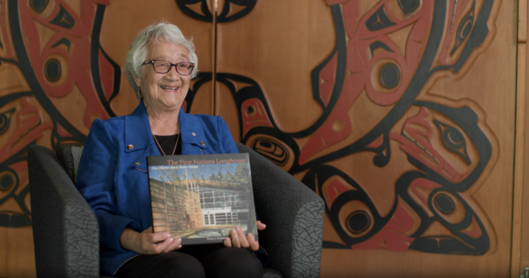 Dr. Verna Kirkness at the First Nations Longhouse, holding a copy of the book she co-authored about the creation of the Longhouse. 