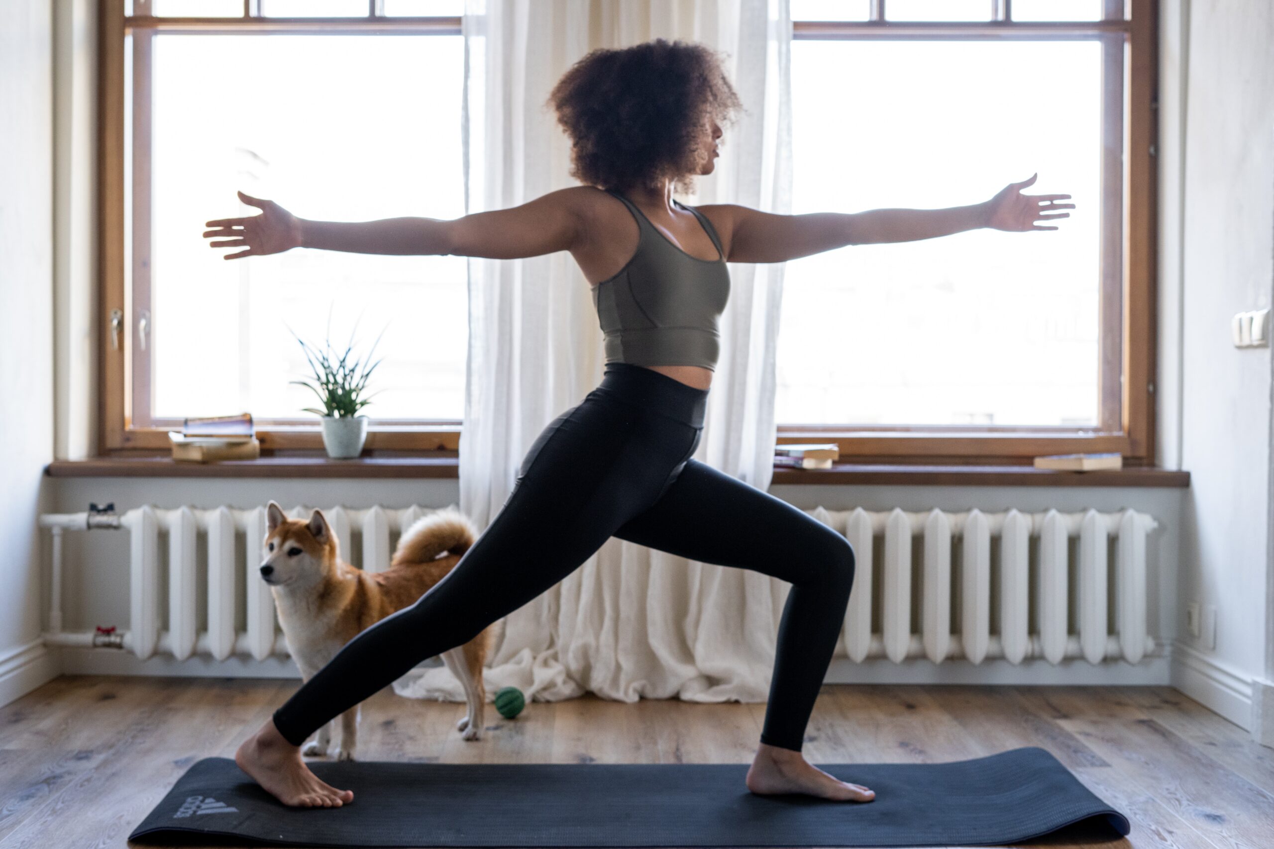 Woman doing a yoga pose in her apartment with a dog in a corner