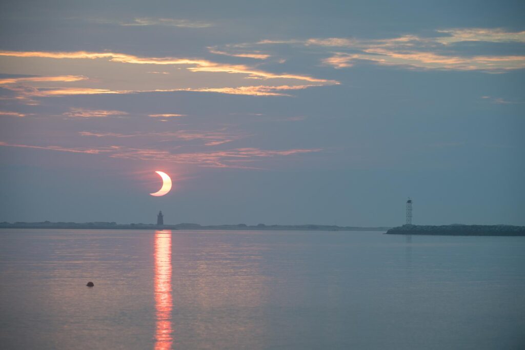 A partial solar eclipse is seen as the sun rises behind the Delaware Breakwater Lighthouse, Thursday, June 10, 2021.
