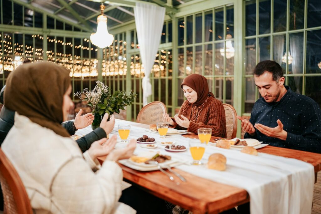 Muslim women and men gathering around a table praying before breaking fast.