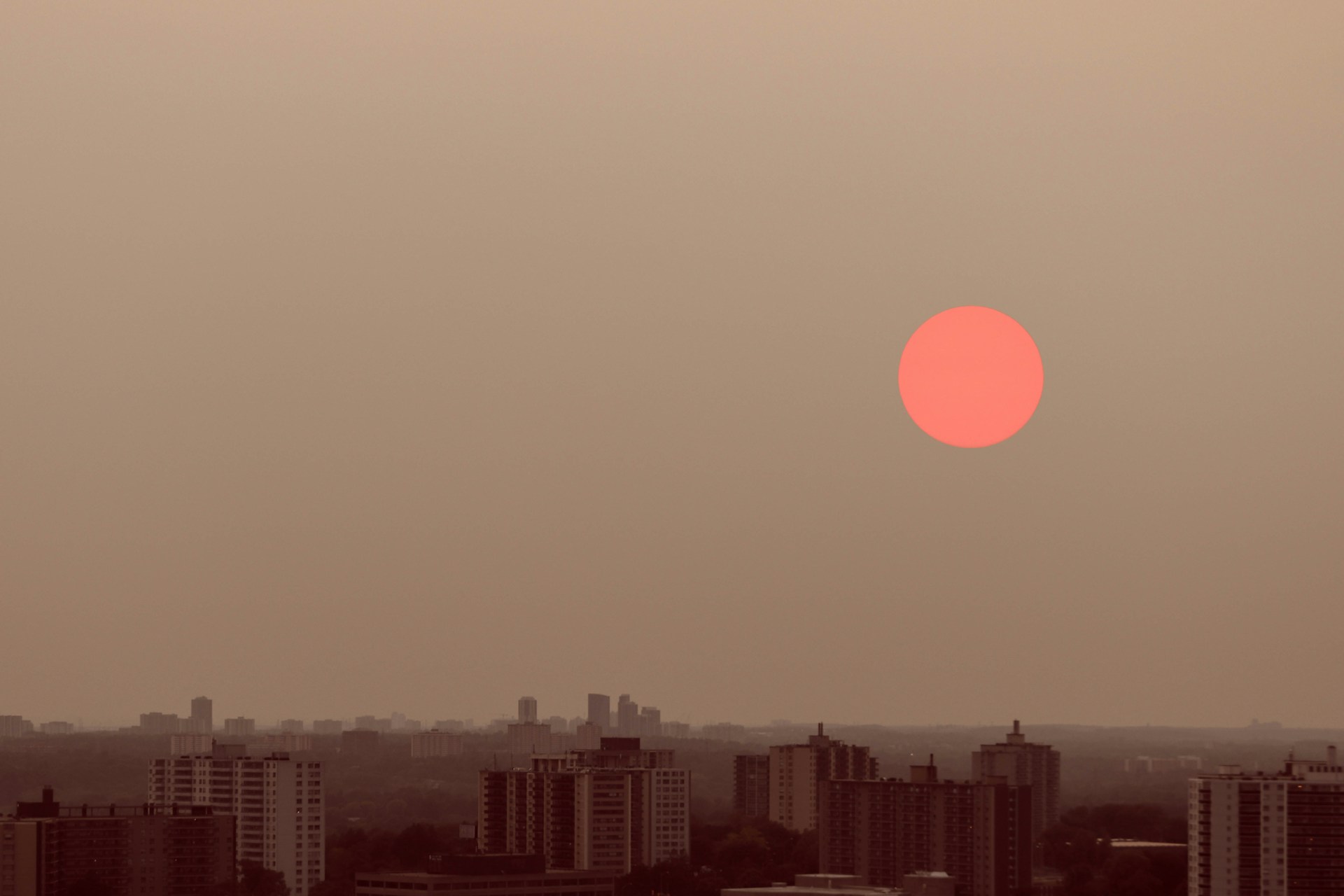 View of the sun which has turned bright red due to wildfires over the Toronto landscape, with hazy skies