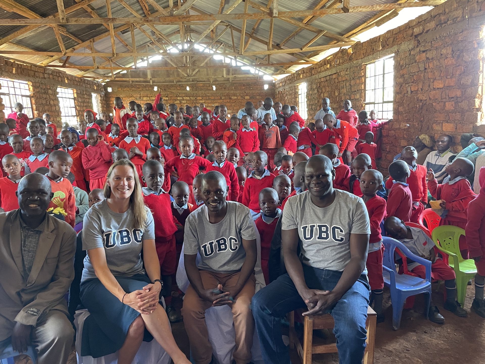 Group photo with Rianyabayo Memorial Academy students in red uniforms, joined by the Academy director, Dr. Sara Beck, Dr. Paul Onkundi Nyangaresi, and another UBC researcher in the foreground.