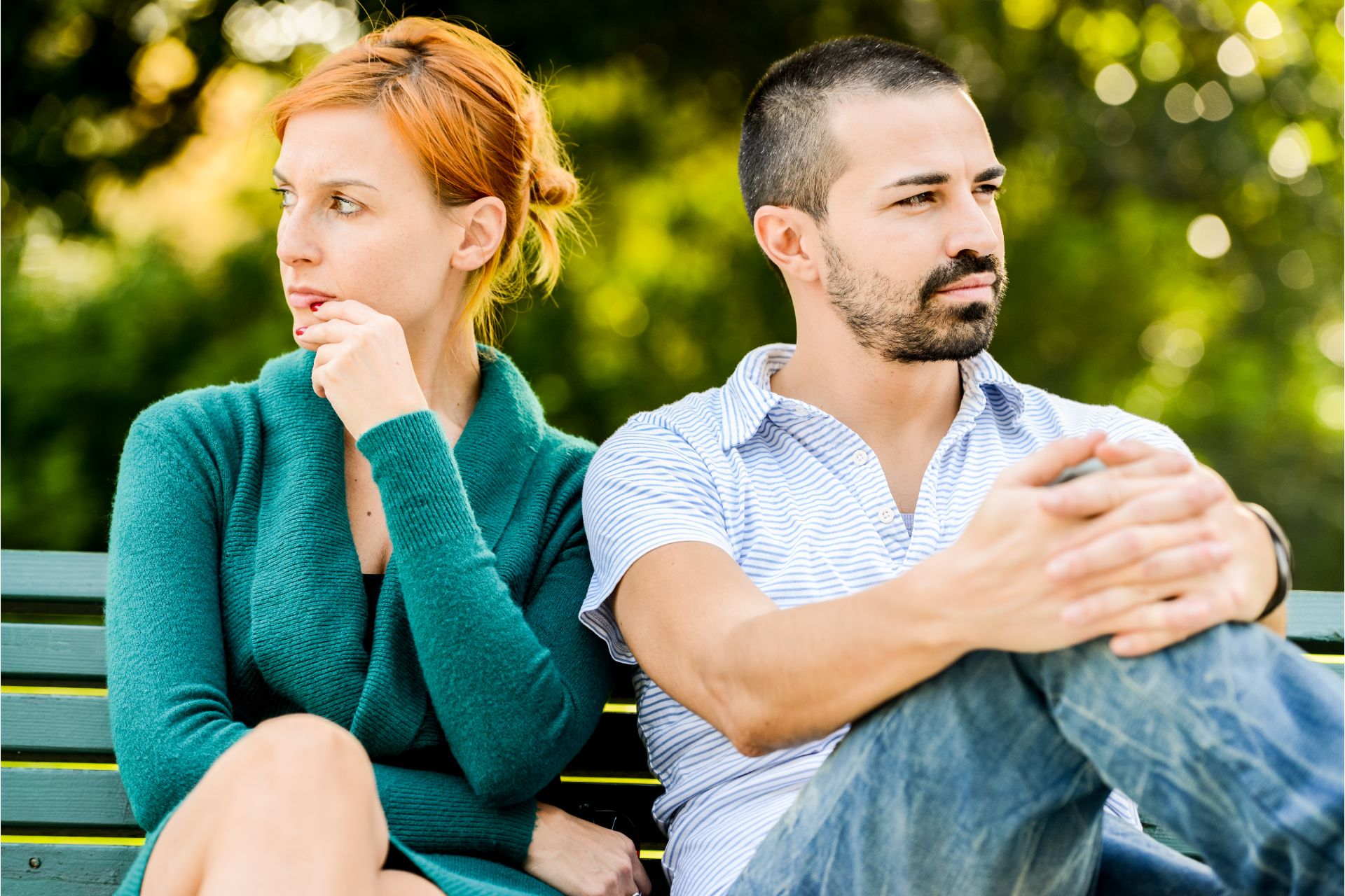 A tense couple sitting apart on a park bench, reflecting conflict in relationships.